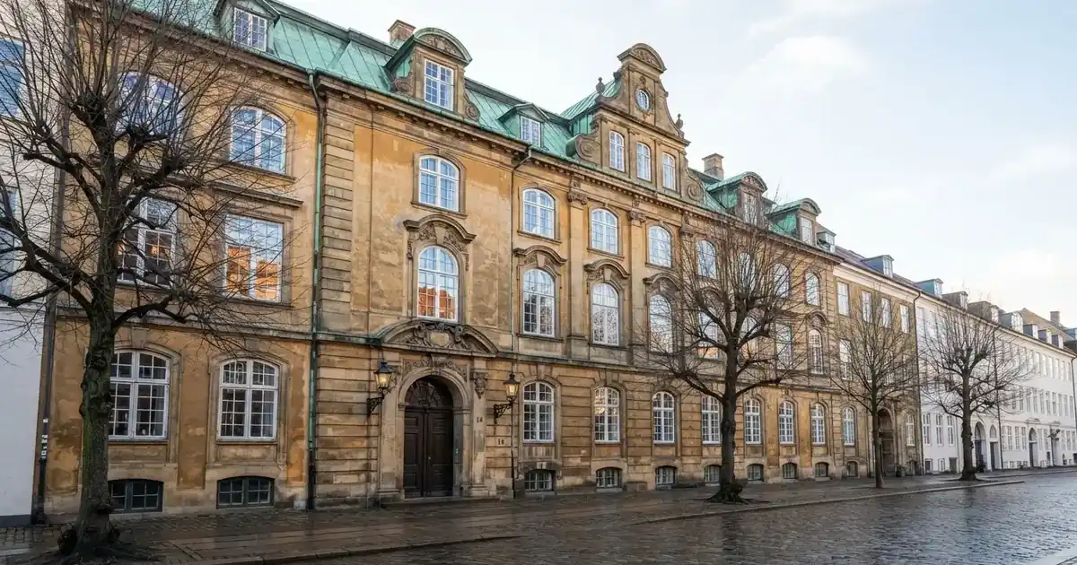 En historisk bygning i København med grønt kobbertag og høje vinduer i klart dagslys, set fra gaden uden mennesker.